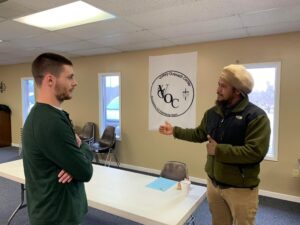 Two men talking over a table with 'Victory Outreach Center' banner in the background